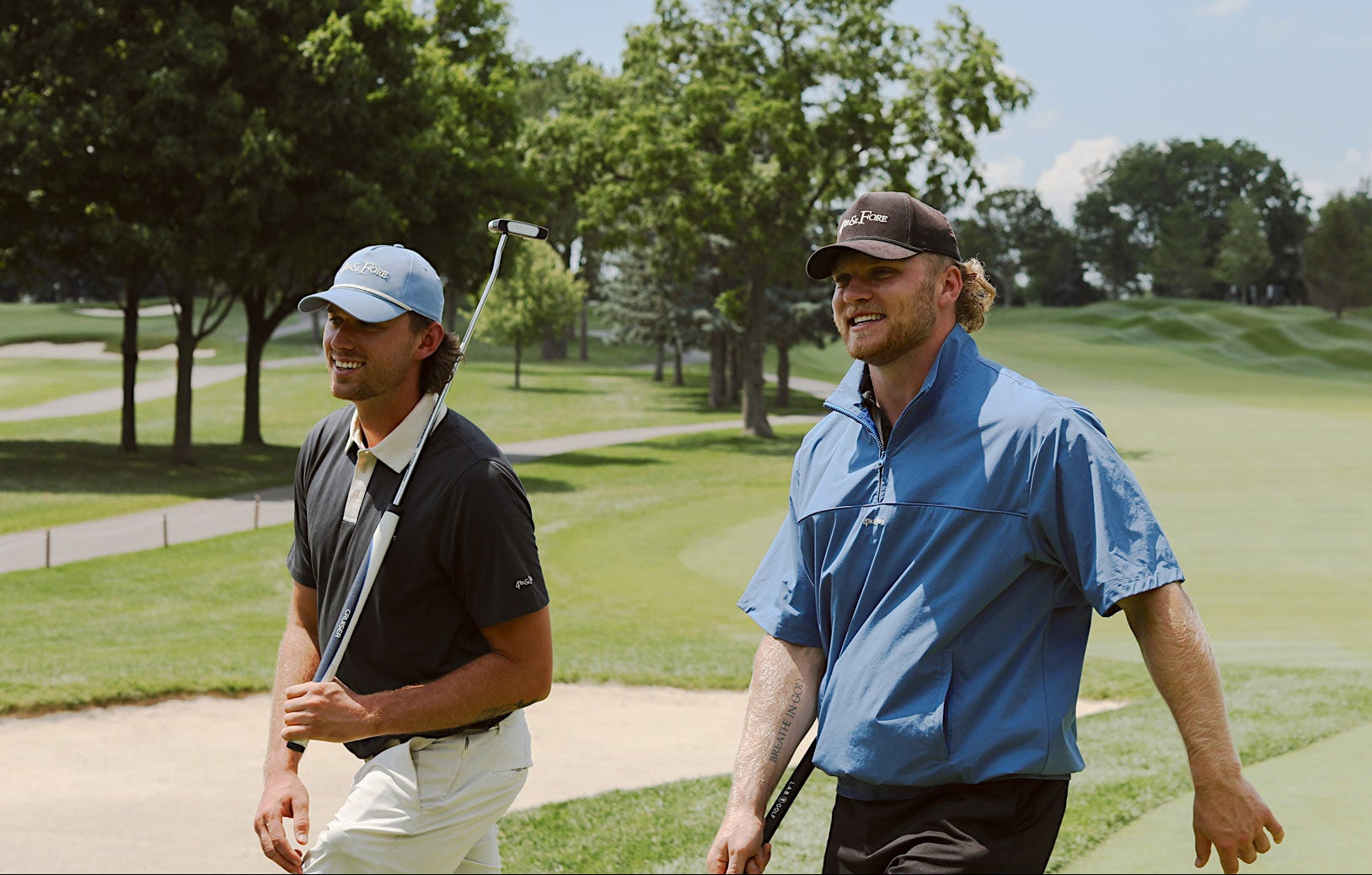 Two players walking off the green in 4th & Fore polos, windshirt and hats